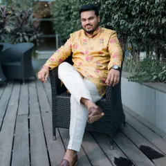 The groom looking relaxed and happy in a vibrant yellow kurta, seated outdoors before the festivities begin.