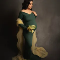 A moment of quiet fulfillment. Holding a delicate bouquet, this mother-to-be looks peaceful and radiant in a classic dark green maternity gown.