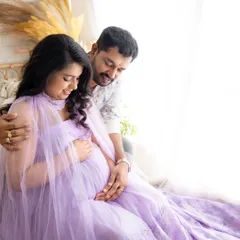 A tender embrace from behind, with the partner looking lovingly at the mom-to-be as she cradles her bump in a beautiful lavender gown.