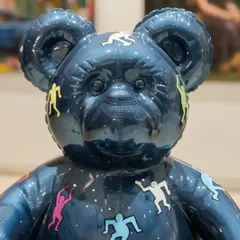 A close-up of the face of 'Ted – Ode To Keith Haring.' The deep blue chrome surface reflects the gallery lights, highlighting the colorful, dancing figures that celebrate joy and freedom.