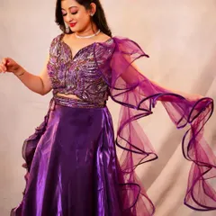 This studio shot focuses on movement and texture. The flowing ruffled sleeve of the purple lehenga creates a dynamic shape, and the detailed embroidery on the blouse is highlighted by the soft studio lighting.