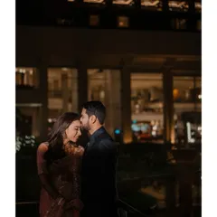 A tender moment captured at night, with the groom gently kissing the bride's forehead. The soft city lights in the background create a beautiful, romantic ambiance.