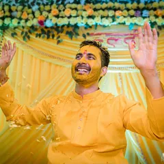 A moment of celebration. The groom, covered in turmeric and rice, raises his hands in the air, embracing the chaos and joy of the ritual.