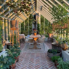 We can design and outfit dedicated garden rooms and greenhouses. This beautiful sunroom features herringbone brick flooring, ample space for a dining set, and is filled with a variety of potted plants, creating a perfect year-round gardening space.