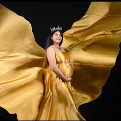 We create magic with fabric. This stunning shot uses a flowing golden satin gown against a solid black background to create a sense of movement and drama, highlighting the beauty of the baby bump.