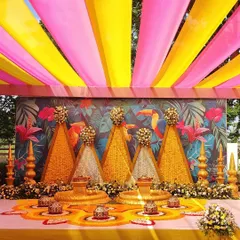 For this outdoor Haldi ceremony, I used a combination of bright pink and yellow fabric draping for the canopy. The backdrop features a custom tropical print, and the stage is decorated with marigold and tuberose floral structures.