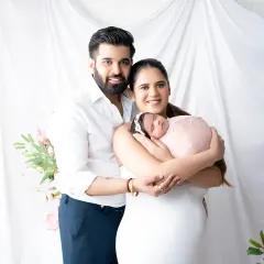 A classic and joyful newborn family portrait. The new parents smile at the camera while holding their precious baby, creating a timeless memory of their complete family.
