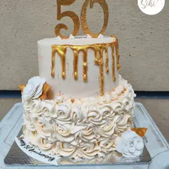 Celebrating a golden anniversary with a cake to match. This two-tiered design for a 50th anniversary features a cascade of buttercream rosettes on the bottom and a beautiful gold drip on top.