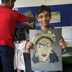 A student smiling with his finished portrait, inspired by traditional Indian performance art. The use of color and detail in the headwear is fantastic.