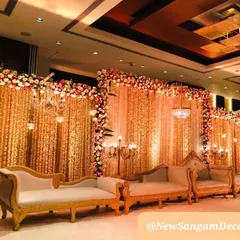 For indoor ballroom weddings, I use elements like this shimmering gold curtain backdrop to add warmth and luxury. The design is framed with a thick border of red and white flowers and accented with classic chandeliers.