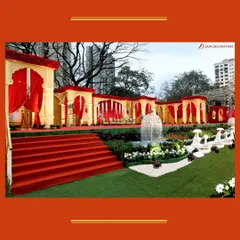 A grand and regal outdoor setup in shades of red and gold. The long arcade of arches and a central fountain create a palatial atmosphere for a traditional wedding.