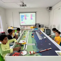 Our training sessions are focused and goal-oriented. This is a typical scene at our North Bangalore center, where students use competition-grade mats and follow structured lessons, like the block-based code on the projector, to prepare for robotics olympiads.