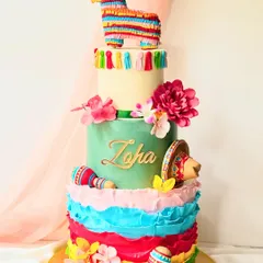 A vibrant four-tiered cake for a Mexican fiesta. The design includes colourful ruffles, a piñata topper, maracas, and a sombrero for a truly festive look.