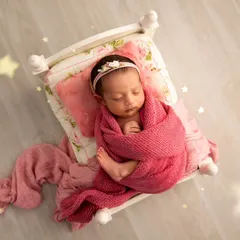 Sweet dreams are made of this. A baby girl is wrapped snugly in pink on a floral-patterned miniature bed, with a soft, dreamy edit that adds a touch of magic.