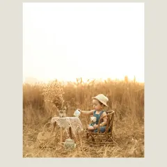 In a playful moment, the child pretends to pour tea during a whimsical picnic in the wheat field. This action shot adds a layer of storytelling and imagination to the outdoor portrait session.