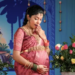A candid shot capturing the wonder of pregnancy. The mom-to-be, adorned in a pink silk saree and gold Oddiyanam, shares a sweet, surprised expression during her baby shower event.