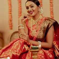 The pure joy of Diwali captured in a warm, ambient portrait. The model, dressed in a beautiful red and gold silk saree, shares a radiant smile, surrounded by the soft glow of diyas, perfectly embodying the festive spirit.