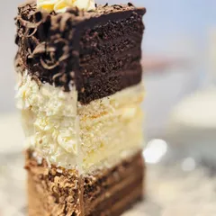 A slice of our signature 24-layer Triple Chocolate Heaven Pastry. It features distinct layers of dark, milk, and white chocolate mousse and sponge, creating an incredible texture and a rich, indulgent experience for any true chocolate lover.