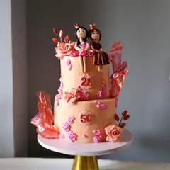 This beautiful two-tiered cake was for a joint birthday celebration for a mother and daughter. It features a peach and rose gold color scheme, handcrafted princess figurines, sugar roses, and delicate rice paper sails.