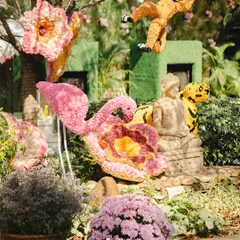 Another view of the whimsical floral animal sculptures, including a pink flamingo and a tiger, set against a lush green background.