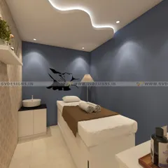 A tranquil massage and treatment room designed for ultimate relaxation. The space features a soothing blue accent wall, soft cove lighting in the ceiling, a dedicated wash basin, and minimalist decor to create an uncluttered and peaceful sanctuary for clients.