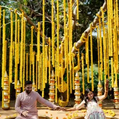 A fun and festive shot of the couple sitting in traditional brass pots during their Haldi ceremony, surrounded by marigold decorations. This captures the unique and playful elements of the celebration.