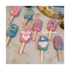 A close-up of my baby shower cakesicles, decorated in pink and blue with cute fondant details like baby clothes and feeding bottles.