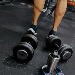 All progress takes place outside the comfort zone. This shot captures the essentials for a great leg day: heavy dumbbells for calf raises, headphones for focus, and a shaker for intra-workout fuel.