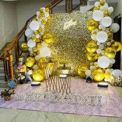 A classic and highly requested setup for birthdays and anniversaries. This features a gold sequin wall, a white and gold organic balloon arch, and custom marquee letters, all brought together with warm uplighting for a celebratory feel.
