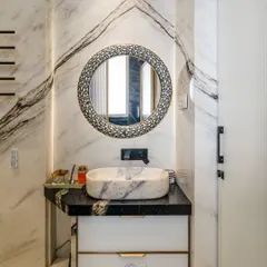 The vanity area is a focal point, with a black granite countertop, a unique marble basin, and an ornate, patterned round mirror that adds a touch of bespoke artistry.