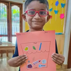 This student proudly displays his "Float & Sink" chart, where he has sorted pictures of objects based on whether they float or sink. This craft activity helps reinforce the concepts learned during our science experiments.