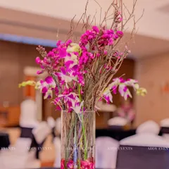 For a modern and artistic touch, we designed this floating floral arrangement. A tall glass vase holds magenta orchids and rustic twigs, creating a centerpiece with height, color, and texture for a chic Sangeet night.