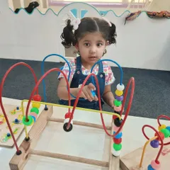 A child concentrates on guiding beads through a wire maze. This classic Montessori activity is excellent for developing hand-eye coordination, fine motor skills, and concentration.
