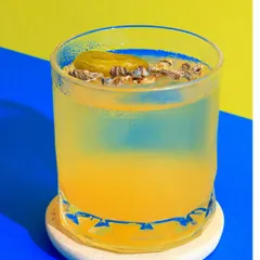 A unique yellow and blue cocktail with a pickled olive garnish, shot with bold colors to highlight its unusual ingredients.