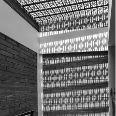 We use architecture to paint with light. Here, a patterned jaali skylight casts intricate shadows on an exposed brick wall, a dynamic display that changes with the sun's journey across the sky. This is how we create spaces that feel active and ever-changing, without using any energy.