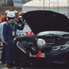 Racers in full gear perform last-minute checks under the hood of a BMW performance sedan. The attention to detail is everything.