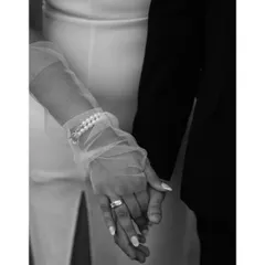 A close-up in black and white, focusing on the couple's intertwined hands. This shot highlights the details: the engagement ring, the delicate gloves, and the simple act of holding on to each other.