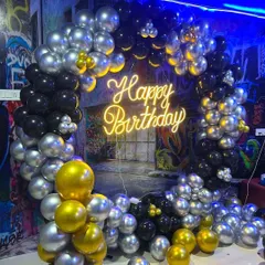 A cool and stylish balloon ring decoration for a birthday, using black, silver, and gold balloons. Set against a graffiti wall, this backdrop with a 'Happy Birthday' neon sign is perfect for a teen or adult party.
