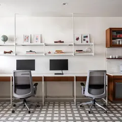 The main workstation area in the 'On The Grid' office is designed for efficiency and collaboration. We used white metal desks with marble tops and ceiling-suspended open shelves to maintain a clean, airy aesthetic, ensuring the 700 sq. ft. space feels uncluttered and productive.
