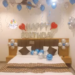 A romantic birthday bedroom decoration with silver 'Happy Birthday' foil letters and balloons on the ceiling and bed.