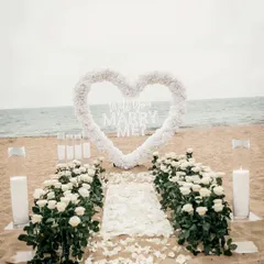 I transform beautiful locations like this beach into a private paradise for your proposal. This elegant setup features a white floral heart, a petal-strewn aisle, and candlelight to create a truly romantic engagement setting.