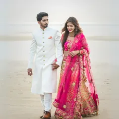 An elegant beach portrait. The couple, dressed in beautiful Indian attire, walks hand-in-hand along the shore, a perfect blend of tradition and natural beauty.