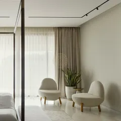 A quiet reading corner in the master bedroom, featuring two cozy, low-level chairs by a large window. The neutral color palette and soft textures make this the perfect spot to unwind.