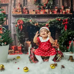 A happy baby girl in her Santa hat, sitting on a plaid blanket amidst a winter wonderland scene. Her joyful expression perfectly captures the spirit of the season.