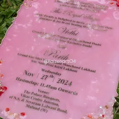 A close-up of a pink resin wedding invitation with an agate-style edge. The gold metal lettering stands out beautifully against the pink base, which is adorned with dried flowers and pearls.
