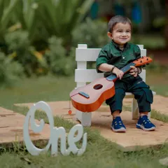 A little musician in the making. This happy moment is from a first birthday photoshoot, where we used a tiny guitar and the "One" sign to capture his cheerful personality. These themed shoots are all about fun.