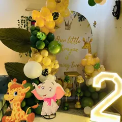 A cute jungle-themed second birthday party. This home setup includes a green and yellow balloon arrangement, character cutouts of a giraffe and elephant, and a large light-up number '2'.