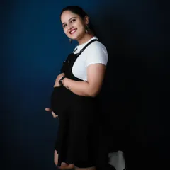 A fun and youthful solo portrait in the studio. The casual dungaree dress and playful pose show that maternity photos can be modern, relaxed, and full of personality.