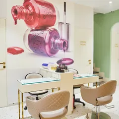 The nail art station is both functional and on-brand, featuring a large, vibrant wall graphic. The quilted chairs and gold-finished table legs add a touch of glamour, reflecting the salon's high-end services.