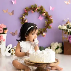 This baby girl is getting right into her first birthday cake during a whimsical butterfly-themed session in the studio.
